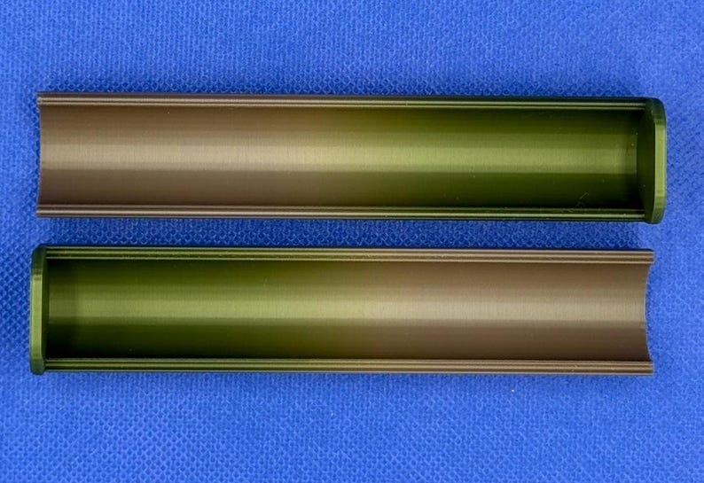 May include: Two metal tubes with a gradient color scheme, transitioning from a dark brown to a light green. The tubes are hollow and have a slightly rounded edge.