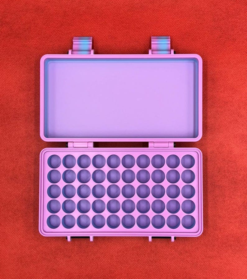 May include: A rectangular light purple storage case with an open lid. The interior base features a grid of forty-eight circular indentations arranged in six rows of eight, designed for holding small items securely within the hard shell container.