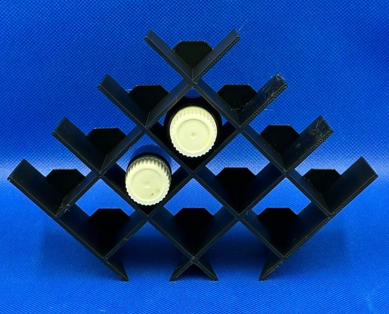 May include: Black plastic rack with 16 slots for storing essential oil bottles. Two white bottle caps are visible in the slots.