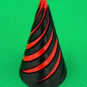 May include: A conical object featuring a spiraling design with alternating black and red layers. The structure tapers to a point at the top and has a wide circular base, showcasing a layered, ribbed texture throughout the entire form.