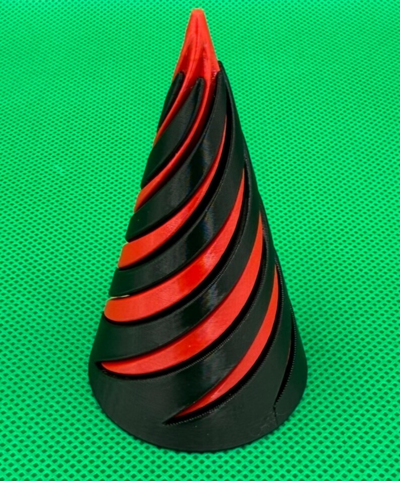 May include: A conical object featuring a spiraling design with alternating black and red layers. The structure tapers to a point at the top and has a wide circular base, showcasing a layered, ribbed texture throughout the entire form.