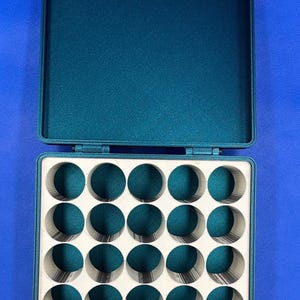 May include: A teal green plastic storage case with a hinged lid and 24 round compartments. The case is open and the compartments are empty.