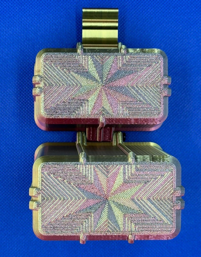 May include: A 3D printed rectangular container with a hinged lid, featuring a metallic gold finish and a multi-colored iridescent star pattern on the top surface. The object has a textured, layered appearance with visible horizontal lines.