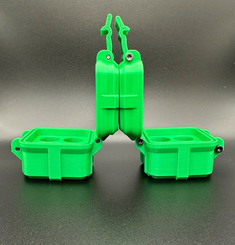 Puede incluir: Un estuche de almacenamiento verde brillante impreso en 3D con dos compartimentos abiertos, cada uno con dos hendiduras circulares interiores. El estuche tiene un mecanismo de tapa con bisagras y pesta&ntilde;as de bloqueo verticales.