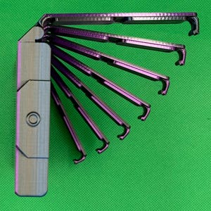May include: A metallic purple multi-tool with a fan-like design, featuring six individual folding arms that extend from a central rectangular handle. Each arm has a hooked end, and the handle displays a circular indentation on its side.