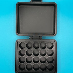 May include: A black rectangular storage case with a hinged lid. The interior base features a grid of twenty circular indentations arranged in four rows of five, while the interior lid is flat and smooth. The case has a textured matte finish.