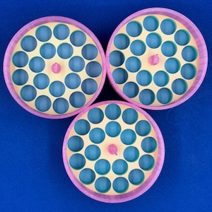 May include: Three circular storage organizers with pink outer rims and light yellow interior trays featuring multiple round holes. Each tray has a small pink center knob and reveals a blue base layer through the circular openings.
