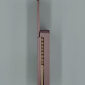 May include: A mauve-colored, rectangular lighter with a hinged lid. The lighter has a vertical, ribbed design on the side and a sliding mechanism. The lid is open, revealing the interior components. The lighter is set against a light blue background.