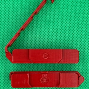 Puede incluir: Dos piezas de pl&aacute;stico rojo que encajan para formar una peque&ntilde;a caja rectangular. La caja tiene un peque&ntilde;o agujero redondo en el centro de la parte superior.
