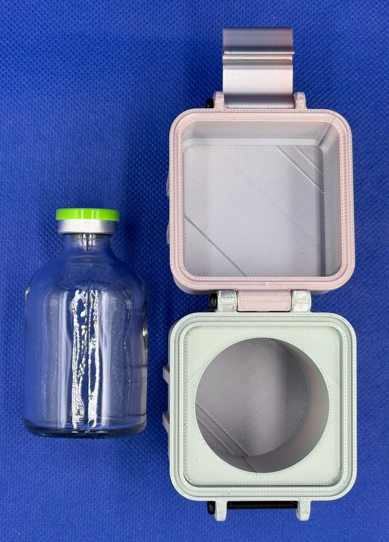 May include: A clear glass vial with a bright green cap sits beside a two-part, 3D-printed square container. The top section is light pink with a square interior, and the bottom section is light green with a circular interior cutout.