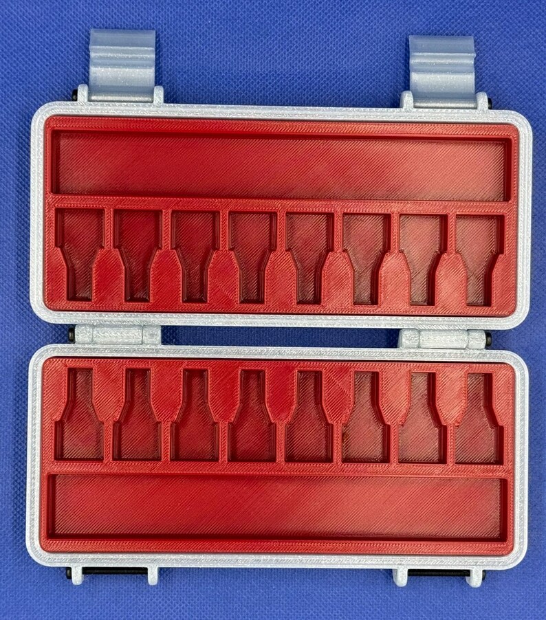 May include: A rectangular storage case with a silver-colored frame and a bright red interior insert. The insert features two rows of eight molded slots designed to hold small items, with a long horizontal compartment above and below each row.