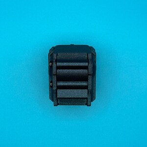 K&ouml;nnte beinhalten: Eine kleine, mattschwarze, rechteckige mechanische Komponente mit einem gerippten Mittelteil aus drei horizontalen Balken und zwei kleinen, kreisf&ouml;rmigen Metallstiften an der linken Seite des strukturierten Geh&auml;uses.