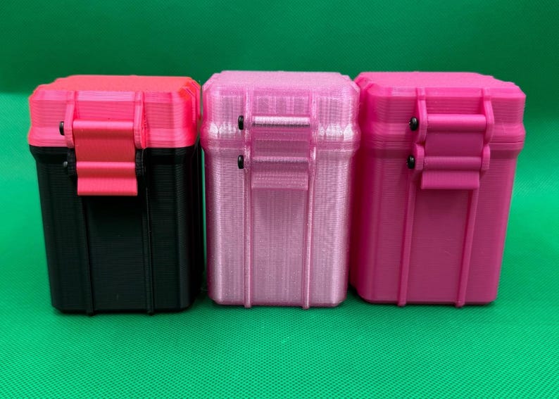 Puede incluir: Tres cajas de almacenamiento rectangulares con tapas abatibles y cierres de pestillo. La primera es negra con tapa y pestillo rosa brillante. La segunda es rosa claro transl&uacute;cido. La tercera es rosa brillante. Todas presentan estr&iacute;as verticales.