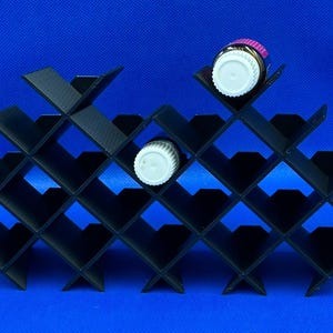 May include: Black plastic organizer with 20 slots in a diamond pattern, designed to hold small bottles. Two bottles are visible, one with a pink cap and one with a white cap.