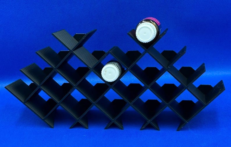 May include: Black plastic organizer with 20 slots in a diamond pattern, designed to hold small bottles. Two bottles are visible, one with a pink cap and one with a white cap.