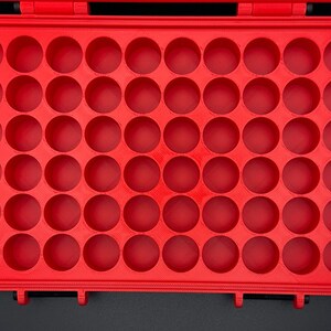 K&ouml;nnte beinhalten: Ein leuchtend roter, rechteckiger Aufbewahrungskoffer mit einem Raster aus sechsundf&uuml;nfzig kreisf&ouml;rmigen, vertieften F&auml;chern. Der Koffer verf&uuml;gt &uuml;ber einen Klappdeckel mit zwei schwarzen Verschl&uuml;ssen an der Unterkante.