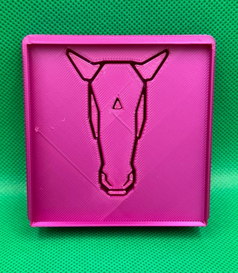 K&ouml;nnte beinhalten: Ein rosa quadratischer 3D-Druck mit einem Pferdekopf-Design in der Mitte.