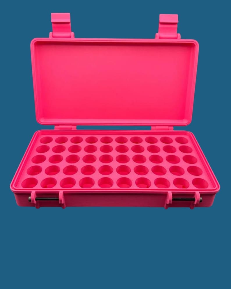 May include: A bright pink rectangular storage case with an open lid, featuring a grid of forty-eight circular indentations for organising small items. The case has two secure latches on the front and two hinges on the back.