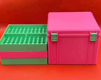 May include: A bright pink storage case with light green latches sits next to a stack of light green storage trays. The trays feature a grid of circular openings designed for organizing small items, while the pink case has a solid lid.