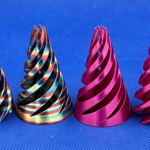 May include: Four conical objects with a spiral, open-lattice design. The two on the left feature a metallic, multi-colored rainbow finish with hues of blue, green, and copper. The two on the right have a solid, vibrant metallic magenta finish.
