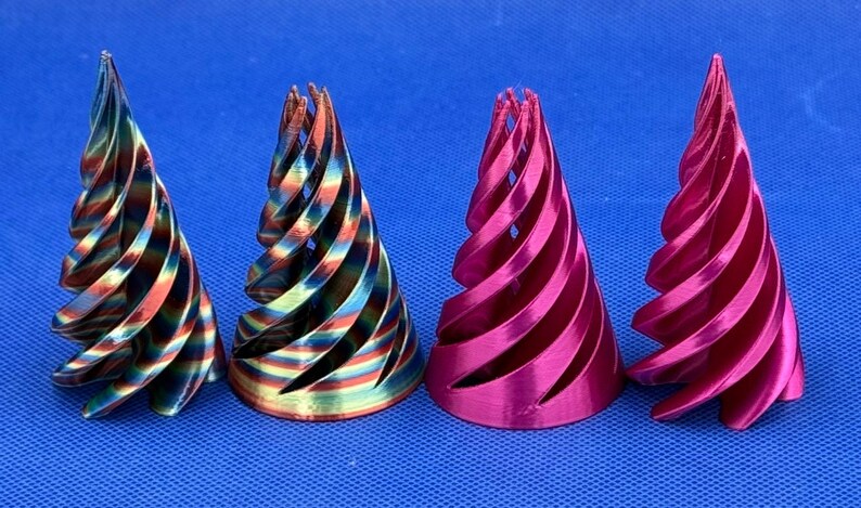May include: Four conical objects with a spiral, open-lattice design. The two on the left feature a metallic, multi-colored rainbow finish with hues of blue, green, and copper. The two on the right have a solid, vibrant metallic magenta finish.