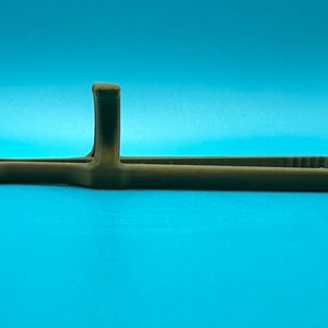 May include: A brown, 3D-printed plastic kitchen tong tool featuring a long, slender design with a central vertical handle support and a looped end. The tongs have a matte finish and a textured surface, with small ridges visible on the gripping tips.