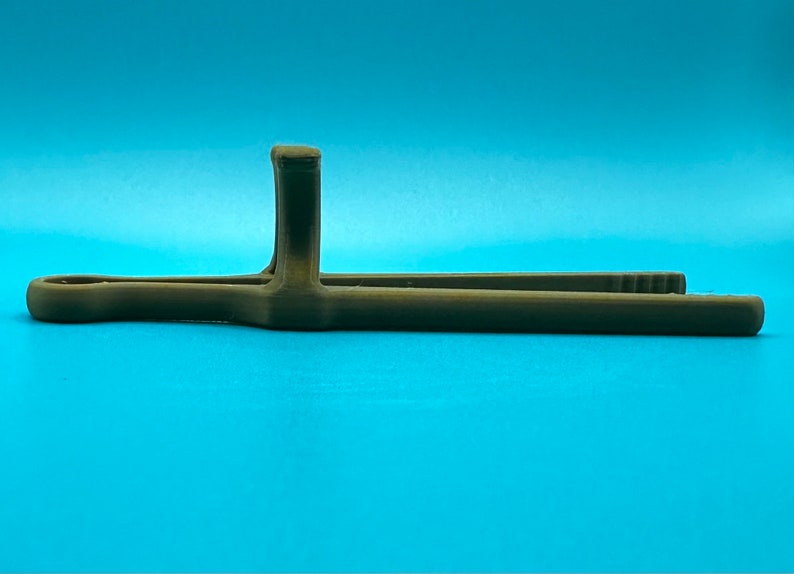 May include: A brown, 3D-printed plastic kitchen tong tool featuring a long, slender design with a central vertical handle support and a looped end. The tongs have a matte finish and a textured surface, with small ridges visible on the gripping tips.