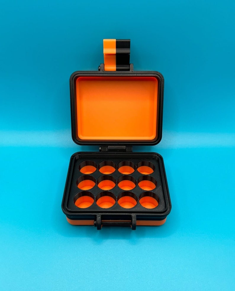 May include: A rectangular black and orange storage case with a hinged lid. The interior features a black tray with twelve circular compartments, each revealing a bright orange base. The exterior latch is coloured in alternating black and orange.