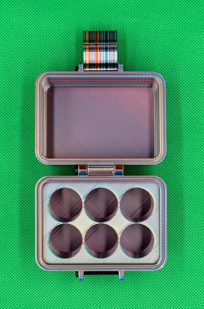 May include: A rectangular, multi-colored, 3D-printed storage case with a hinged lid. The interior features a flat compartment on the top half and six circular recessed slots on the bottom half. The case displays a layered, iridescent finish.