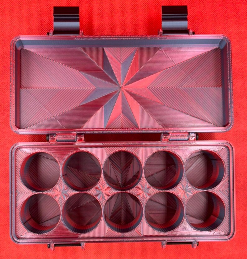 Puede incluir: Un estuche de almacenamiento rectangular de color rojo oscuro impreso en 3D con tapa abatible. El interior de la tapa presenta un patr&oacute;n de estrella geom&eacute;trico, mientras que la base contiene diez compartimentos circulares dispuestos en dos filas de cinco, todos con un acabado texturizado.