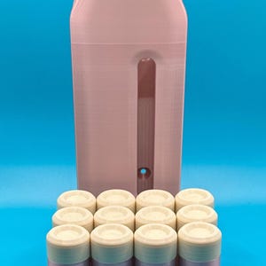 May include: A light pink vertical storage unit with a central slot and a small circular hole at the bottom, positioned behind a grid of eight small, cylindrical containers with off-white lids and light pink bases arranged in two rows.