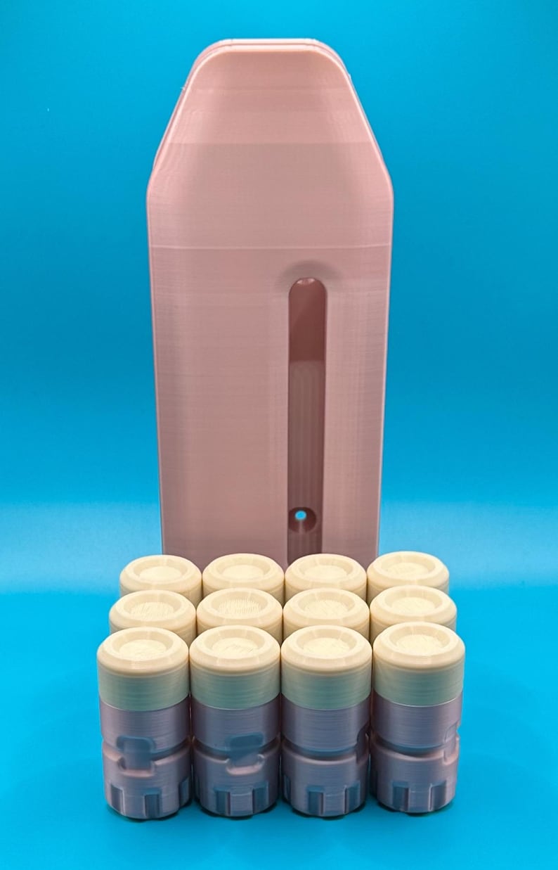 May include: A light pink vertical storage unit with a central slot and a small circular hole at the bottom, positioned behind a grid of eight small, cylindrical containers with off-white lids and light pink bases arranged in two rows.