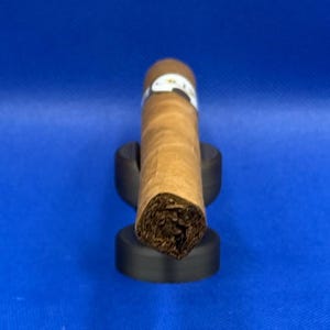 May include: A brown cigar with a white band is resting on a black cigar holder.