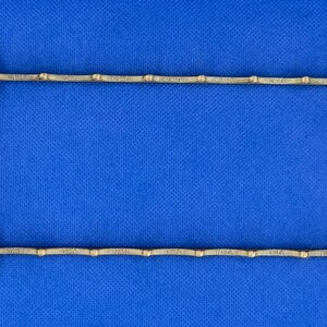 K&ouml;nnte beinhalten: Ein goldfarbener Metallrahmen mit rechteckiger Form. Der Rahmen hat eine Reihe von kleinen, gleichm&auml;&szlig;ig verteilten, runden Dekorelementen entlang der oberen und unteren Kante.