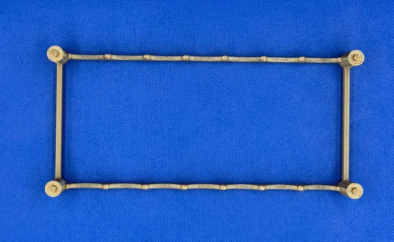 K&ouml;nnte beinhalten: Ein goldfarbener Metallrahmen mit rechteckiger Form. Der Rahmen hat eine Reihe von kleinen, gleichm&auml;&szlig;ig verteilten, runden Dekorelementen entlang der oberen und unteren Kante.