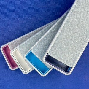 May include: A set of four rectangular cases with silver glitter textured lids. Each case features a distinct interior color: magenta, white, bright blue, and dark blue. The cases are arranged in a fanned-out, overlapping diagonal formation.