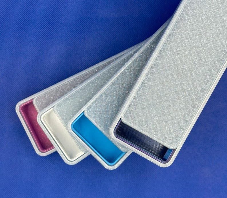 May include: A set of four rectangular cases with silver glitter textured lids. Each case features a distinct interior color: magenta, white, bright blue, and dark blue. The cases are arranged in a fanned-out, overlapping diagonal formation.