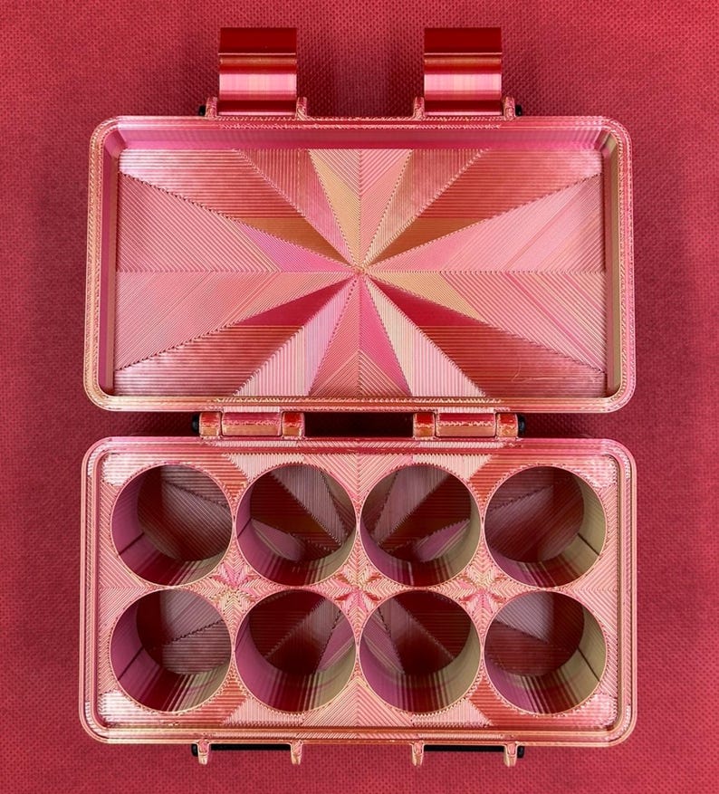 May include: A red plastic storage box with a hinged lid and six round compartments. The box has a geometric pattern on the lid and the compartments.