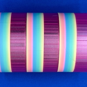 May include: A cylindrical object featuring a repeating pattern of vertical stripes. The design consists of alternating bands of solid deep purple and a gradient transition of soft pink, light blue, and pale yellow colors.