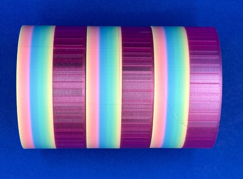 May include: A cylindrical object featuring a repeating pattern of vertical stripes. The design consists of alternating bands of solid deep purple and a gradient transition of soft pink, light blue, and pale yellow colors.