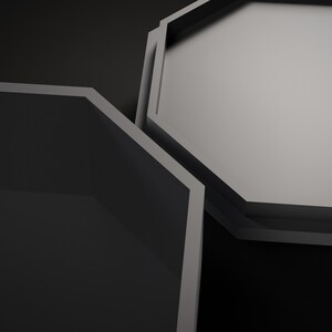May include: Two octagonal containers with a matte finish. One container is open and empty with dark interior walls, while the other is positioned slightly above it, showing a light gray, flat, solid octagonal lid or base surface.