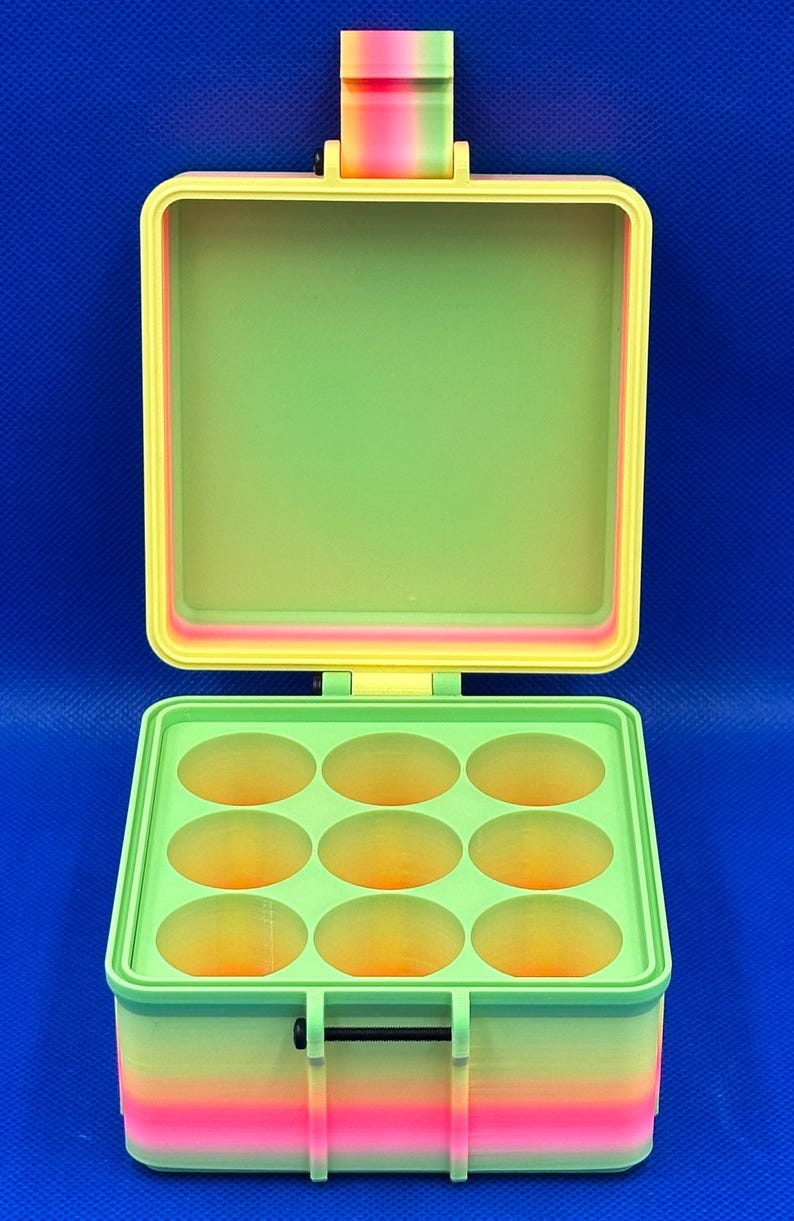 May include: A square, hinged storage container featuring a gradient color scheme of pink, orange, yellow, and green. The interior base contains nine circular compartments arranged in a three-by-three grid, while the lid remains open.