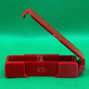 Puede incluir: Una caja de pl&aacute;stico roja con bisagras y dos compartimentos. La caja est&aacute; abierta y la tapa est&aacute; articulada en la parte posterior.