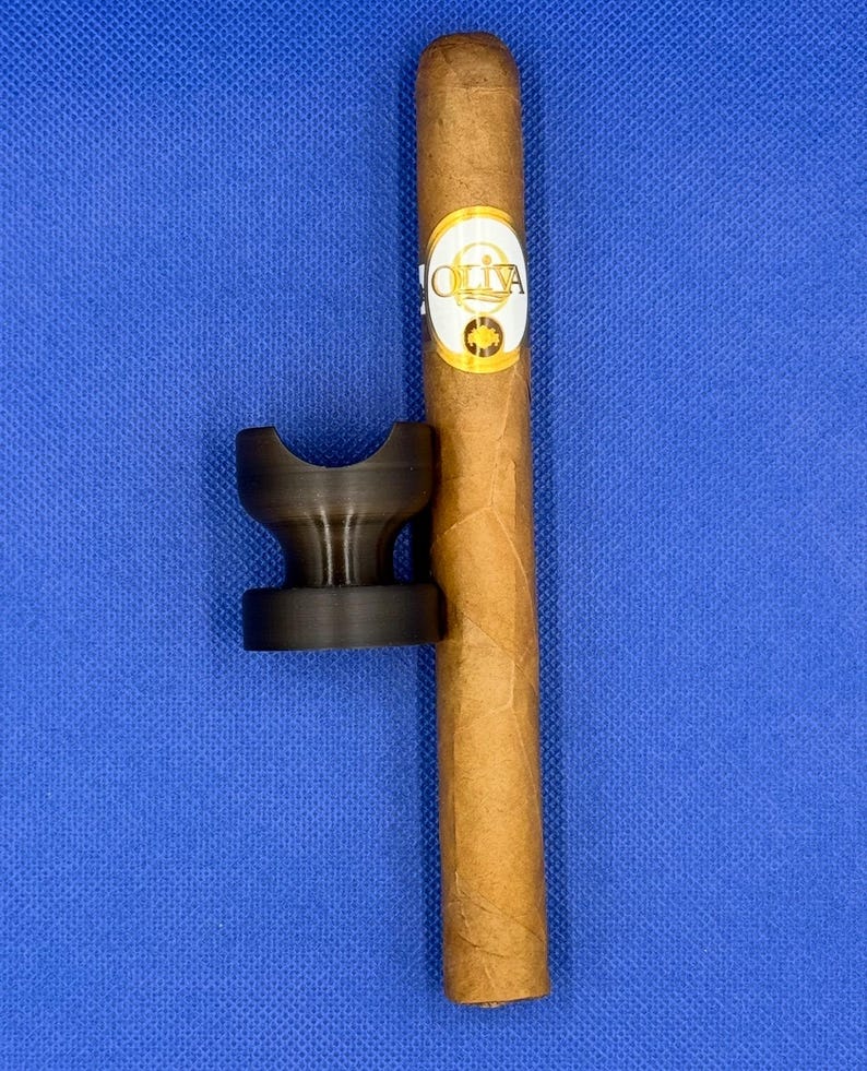 May include: A brown cigar with a gold band that says "OLIVA" on a blue surface with a black cigar rest.