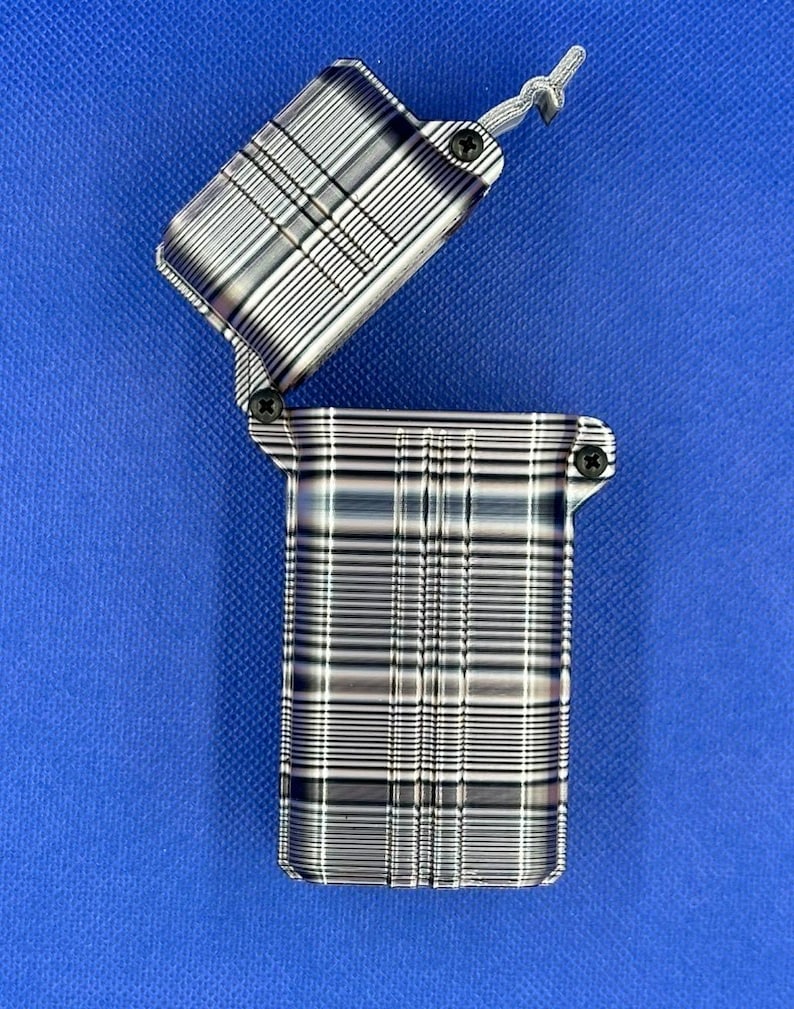 May include: A rectangular metal lighter with a hinged lid in an open position. The surface features a metallic finish with a repeating pattern of horizontal and vertical lines in shades of silver, gray, and black. Two small black screws are visible.