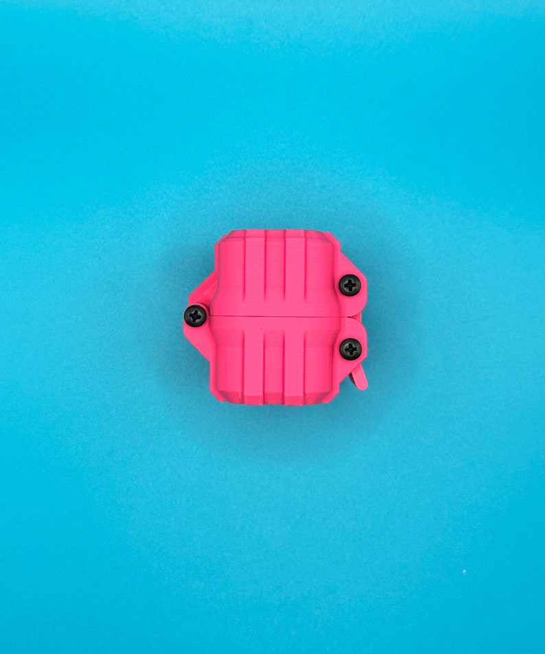 May include: A bright pink, rectangular, ribbed plastic case featuring three visible black Phillips head screws securing the two halves together. The object has a structured, industrial appearance with vertical grooves along its surface.