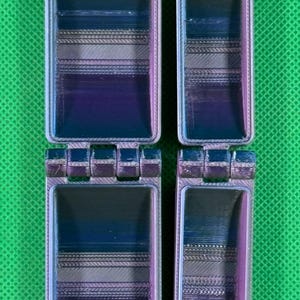 May include: Two small, hinged, rectangular boxes with a multi-coloured, iridescent finish. The boxes are made of plastic and have a textured surface.