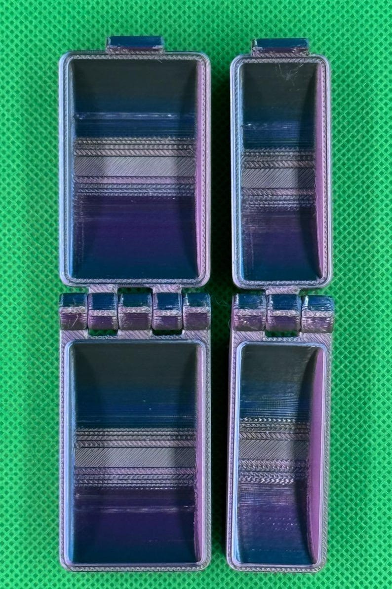 May include: Two small, hinged, rectangular boxes with a multi-coloured, iridescent finish. The boxes are made of plastic and have a textured surface.