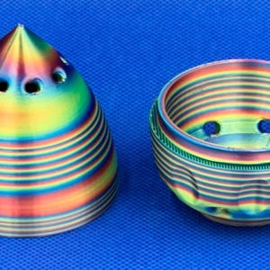 May include: Two 3D printed objects, a cone and a bowl, with a rainbow iridescent finish. Both objects have multiple holes in the top.