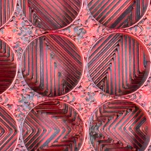 May include: Close-up of a red and black textured surface with a repeating pattern of circular indentations. The surface has a rough, almost metallic look.